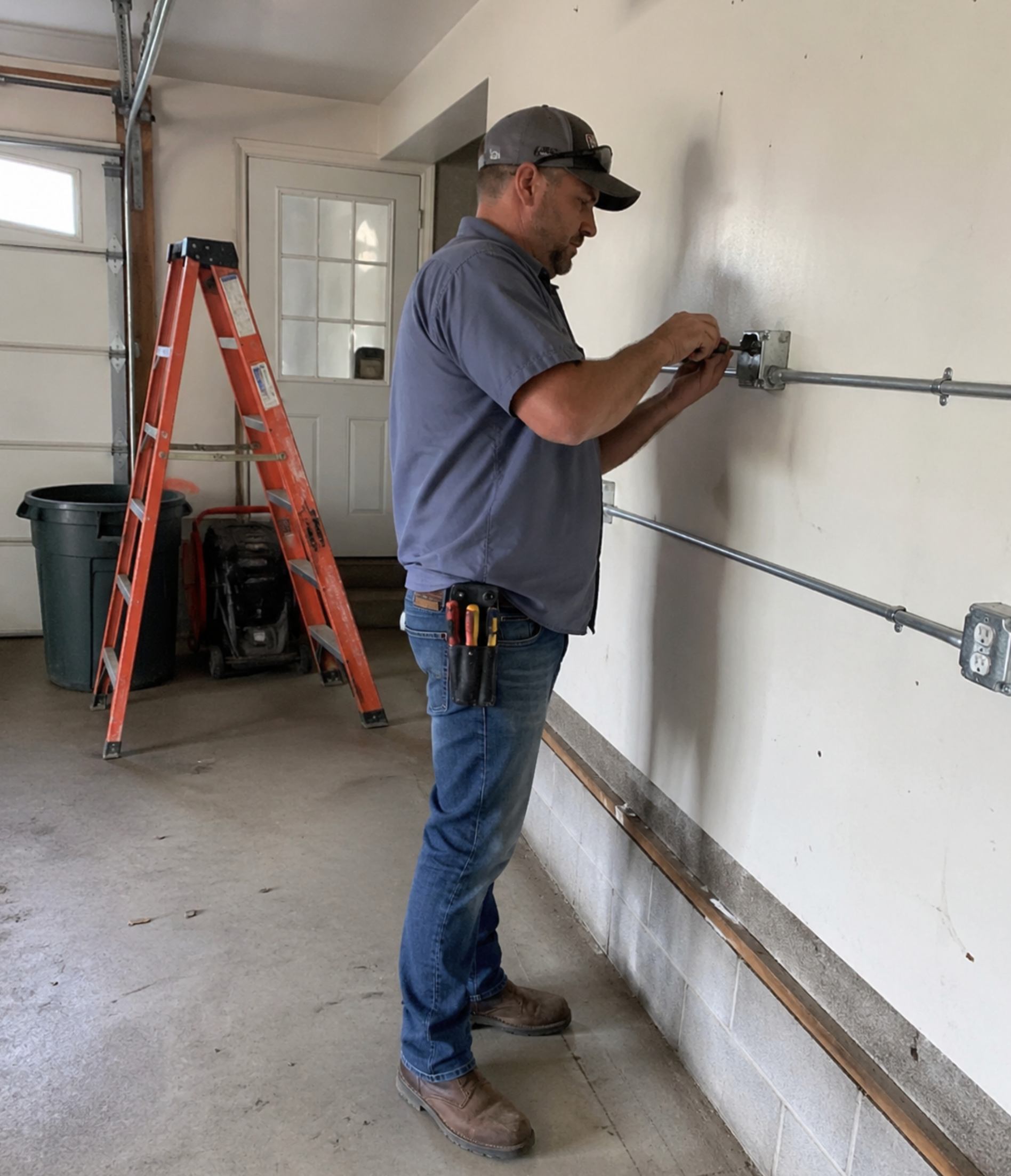 Electrician installing outlet in garage with ladder and tools